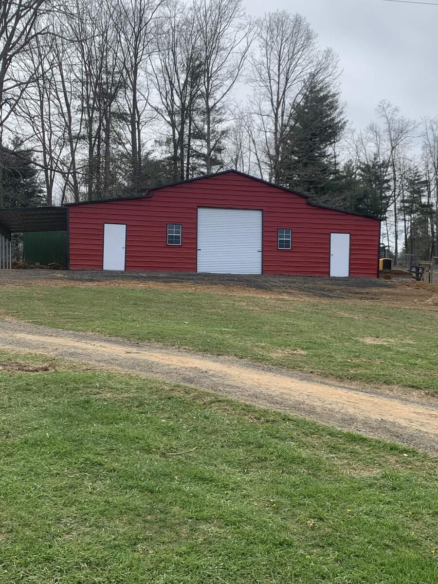 Red metal barn with a roll-up door, two walk-in doors, two windows, and an open lean-to on one side