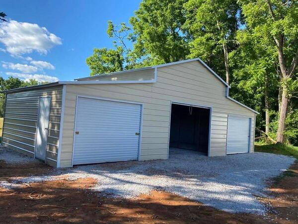 Tan metal barn with white trim, a raised center section, lean-tos on both sides, and three roll-up doors