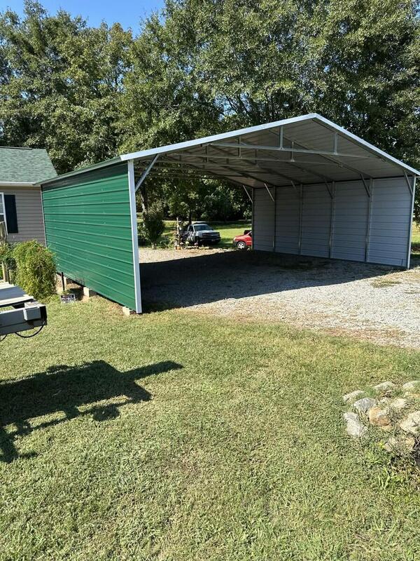 Metal carport with a green side wall, gray paneling on the far side, and an open front over gravel