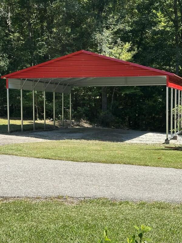 Open-sided metal carport with a red roof and trim over a gravel pad