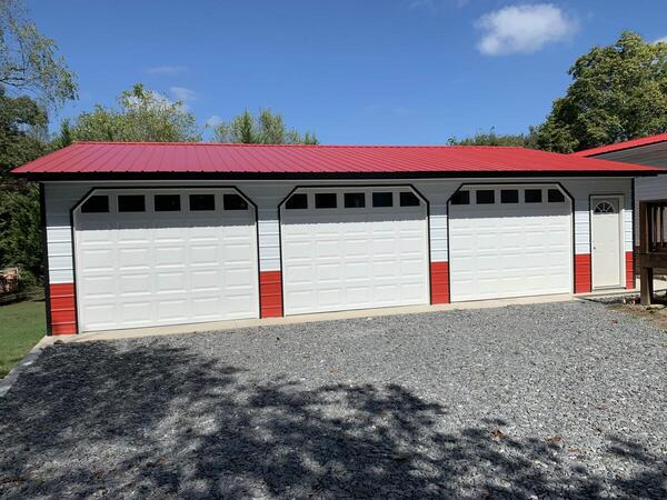 White three-car metal garage with a red roof, three raised-panel garage doors, and a walk-in door