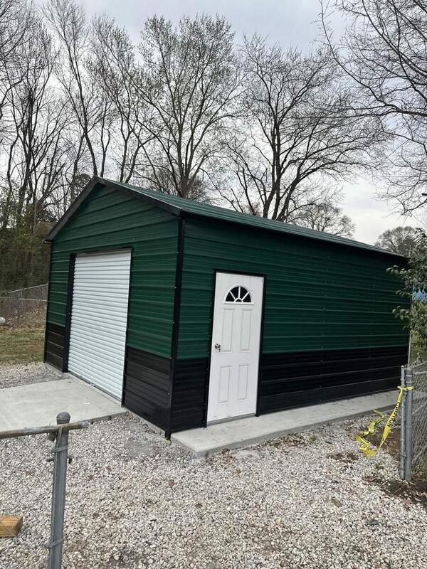 Green metal garage with black lower panels, a white roll-up door, and a walk-in door