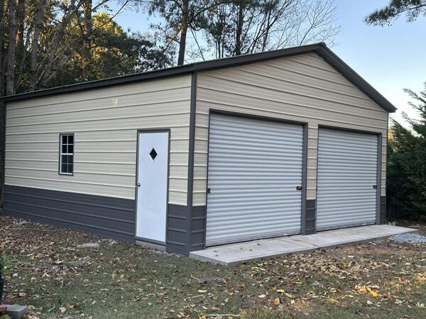 Tan metal garage with gray lower panels, two roll-up doors, a walk-in door, and a window