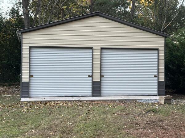 Front of a tan and gray metal garage with two roll-up doors on a concrete apron