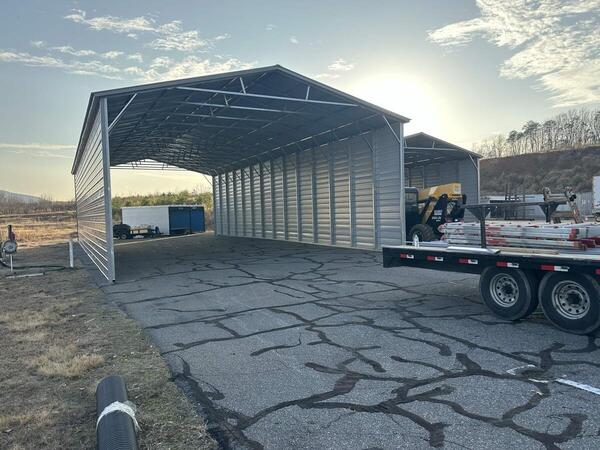 Two tall metal covers with vertical roofs, closed sides, and open ends on an asphalt lot